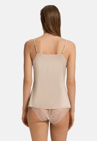 Nude top na ramiączkach z cienkimi, regulowanymi paskami, wykonany z gładkiego materiału. Charakteryzuje się luźnym krojem. Połączony z dolną częścią z koronkowymi detalami, prezentującą wzory kwiatowe.
