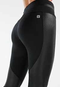 Leggings noirs en matériau lisse et extensible avec un design élégant, comportant un petit logo, des lignes de contour et une taille haute.