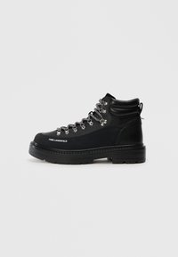 Botas de senderismo negras con parte superior de cuero texturizado, herrajes plateados y cordones grises. Presenta una suela robusta y un tobillo acolchado para mayor soporte.