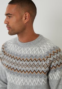 Grijze gebreide trui met een geometrisch patroon in wit, bruin en donkergrijs. Ronde halslijn en textuurstof.