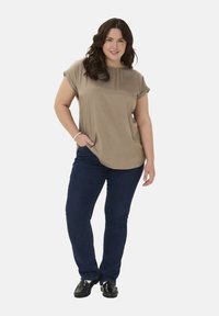 Kortærmet olivengrøn bluse med rund halsudskæring, parret med mørkeblå skinny jeans og sorte sko med dekorative detaljer.