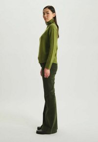 Pull vert en tricot à col roulé associé à un pantalon évasé en corduroy vert assorti, avec une texture côtes et une finition lisse. Chaussures noires.