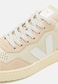 Beige og kremfargede sneakers laget av lær og semsket skinn, med en hvit logo, perforert tå og lys grå lisser. Teksturerte gummis�åler.