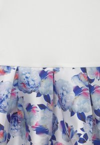 Vitt tygplagg med en plisserad nederkant som har blå och rosa blomstermönster samt mörkblå blad.