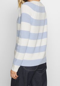 Maglione a righe blu e bianche con scollo rotondo, texture a coste e maniche lunghe, abbinato a pantaloni scuri.