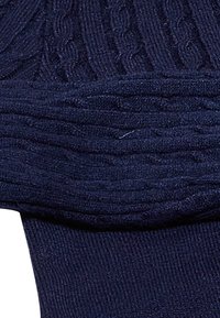 Secțiune de pulover tricotat bleu navy, cu modele de cabluri și cusături rib. Textură moale, detalii vizibile în cusăturile ridicate.