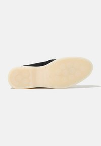 Scarpa nera con suola piatta in gomma, dotata di una grip a disegno e un battistrada di colore crema. Il marchio è impresso sulla suola.