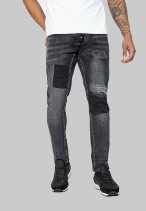 Jean en denim noir avec des détails en patchwork, des zones effilochées et une coupe slim. Assortis avec des chaussures de sport noires.