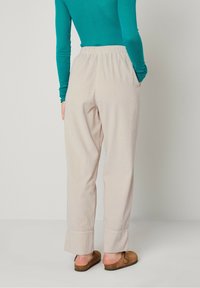 Lichtbeige gestreepte broek met een ontspannen pasvorm, elastische tailleband, zijzakken en licht uitlopende manchetten, gecombineerd met een turquoise blouse met lange mouwen.