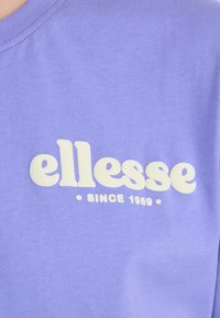 Purple cotton t-shirt featuring a large white "ellesse" logo and "SINCE 1959" text positioned centrally on the chest. Soft texture.
