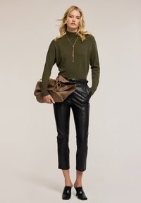 Zielony sweter z golfem, czarne krótkie spodnie z ekologicznej skóry, beżowa torebka z miękkiego materiału z złotymi akcentami oraz czarne sandały z odkrytymi palcami.