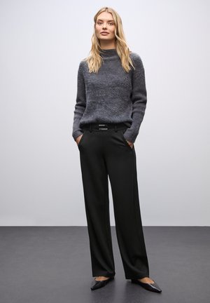 Gray knit sweater with a high neckline, paired with black wide-leg trousers featuring a sleek belt, set against a neutral background.