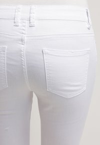 Jeans de mezclilla blanca con una textura suave, corte ajustado, cinturilla estándar y dos bolsillos traseros de forma rectangular.