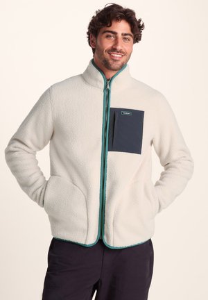 Fleece jacket in cream with teal zipper and hem. Features a dark blue chest pocket with a logo. Side pockets and a high collar.