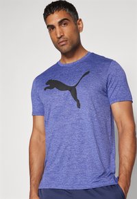 Sinine spordit-särk, mis on valmistatud tekstureeritud kangast, mille rinnal on silmapaistev must Puma logo. Lühikesed varrukad ja ümmargune kaelus.
