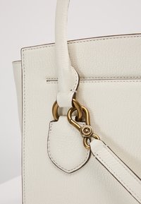 Biała skórzana torebka o teksturowanym wykończeniu, z klamrą w złotym kolorze i odczepianym paskiem. Czyste linie i minimalistyczny design.