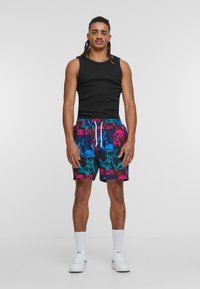 Black tank top, colorful patterned swim shorts featuring pink, blue, and black designs. White drawstring and white socks with sneakers.