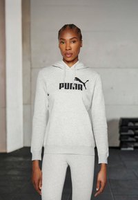 Svetlošedá mikina s kapucňou a čiernym logom "PUMA" a dizajnom mačky, so šnúrkou na kapucni a rebrovanými manžetami, v kombinácii s koordinačnými legínami.