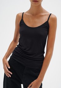 Top nero senza maniche realizzato in tessuto morbido ed elastico, caratterizzato da sottili spalline e scollo rotondo. Il design è aderente con delicate arricciature sui lati.