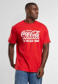 Rød bomulds T-shirt med hvid Coca-Cola logo tekst. Korte ærmer og en afslappet pasform med ternet mønster under teksten.