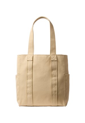 Beige Calvin Klein lærredstaske med to lange håndtag, lodret broderet brandnavn på forreste stropper og sidelommer.