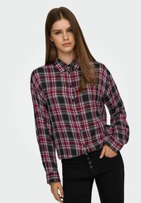 Långärmad rutiga skjorta i svart, röd och vit; har en knapp-down krage och knappar längs framsidan, kombinerad med svarta högmidjade jeans.