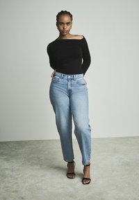 Haut noir à manches longues avec un design décolleté, associé à un jean droit taille haute bleu clair et des talons noirs à lanières.