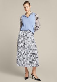 Lichtblauwe mouwloze sweater over een gestreept overhemd met kraag. Vloeiende geplooide rok met een geometrisch dessin in blauw, wit en zwart.