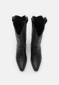 Botas de vaquero de cuero negro con punteras puntiagudas, costuras decorativas y pestañas en la parte superior. Textura suave y diseño elegante.