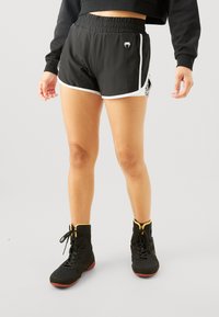 Shorts de sport noirs avec des bordures et un logo blancs, présentant une coupe ample et une taille élastique. Associés à des baskets montantes noires et respirantes.