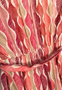 Robe à imprimé floral présentant un motif de feuilles roses et beiges sur un fond clair, avec une taille froncée et une ceinture assortie.