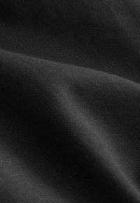 Tissu noir texturé avec une surface lisse, présentant des variations subtiles d'épaisseur qui créent de la profondeur et une apparence douce et ondulante.