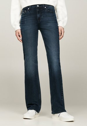 Vaqueros de mezclilla azul oscuro de pierna acampanada con una cintura de altura media, diseño de cinco bolsillos y costuras en contraste, complementados con un suéter blanco de canalé y zapatillas.