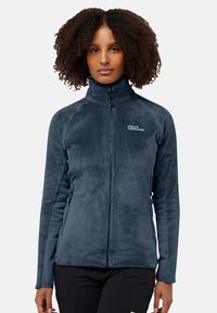 Giacca in pile blu navy con colletto alto, chiusura con zip e tasche laterali. Tessuto morbido con pannelli a contrasto elasticizzati e dettaglio del logo sul petto.