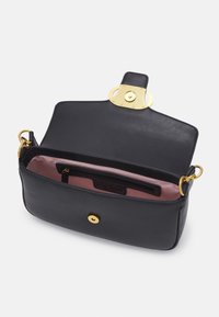 Sac à main en cuir noir avec garnitures dorées, rabat ouvert montrant la doublure intérieure rose et une poche zippée intérieure.