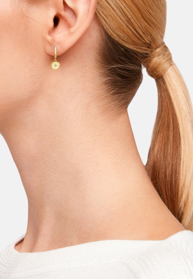 Orecchino ad a mpolla in oro con un piccolo ciondolo circolare con design di stella in rilievo, appeso a un gancio a leva. La superficie è liscia.