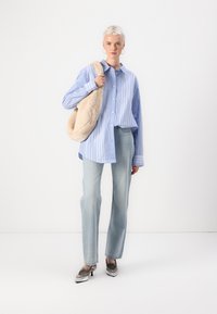 Ljusblå och vit randig oversized knapplös skjorta, ljus tvättade jeans, metalliska klackskor och en mjuk beige tote-väska.