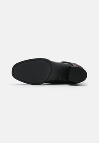 Semelle de chaussure en cuir noir avec un design plat, texture lisse, et nom de marque embossé, dotée d'un motif de grip en caoutchouc pour l'adhérence.