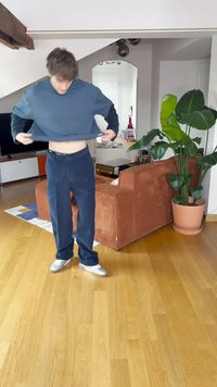 Σκοτεινό μπλε κοντό sweatshirt, σε άνετη γραμμή, συνδυασμένο με ναυτικές παντελόνες. Ξύλινο πάτωμα και πράσινο γλάστρα φυτού σε έναν μοντέρνο εσωτερικό χώρο.