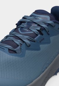 Μπλε αθλητικό παπούτσι με υφή, μπλε κορδόνια με σχέδιο, μαξιλαρωμένη γλώσσα με την επιγραφή "ALTRA TIMP 6" και ενισχυμένες οπές κορδονιών.