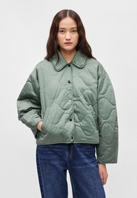 Κουβερλί, πράσινο μπουφάν με γιακά, κλείσιμο με κουμπιά και πλάγιες τσέπες. Διαθέτει υφή με σχέδιο κύματος.