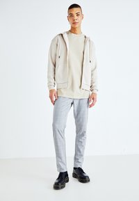 Sudadera beige con cremallera sobre una camiseta beige, combinada con pantalones ajustados de cuadros grises y botas negras con cordones y suela gruesa.