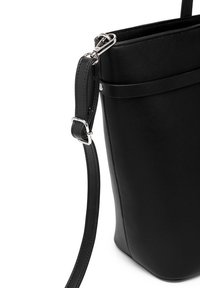 Černá kožená kabelka přes rameno s hladkým povrchem, obdélníkovým tvarem a stříbrnými detaily. Má nastavitelný popruh a minimalistický design.
