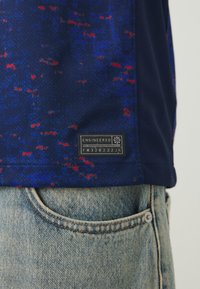 Camicia a maniche corte di colore navy con un motivo a macchie blu e rosse, caratterizzata da un'etichetta nera con la scritta "ENGINEERED" nella parte inferiore.