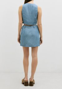Denim-Crop-Top- und Rock-Set, hellblaue Farbe, figurbetontes Design. Der Rock ist knielang mit einer definierten Taille und Gürtelschlaufen.