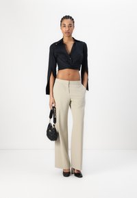 Crna skraćena majica s otvorenim rukavima, bež široke hlače, crna torba s logom na remenu i crne cipele s visokim potpeticama.