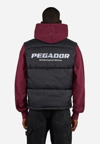 Černá péřová vesta s vínovým mikinou s kapucí pod ní. Obsahuje bílé logo "PEGADOR" a text "CERTIFIED AUTHENTIC STREETWEAR".