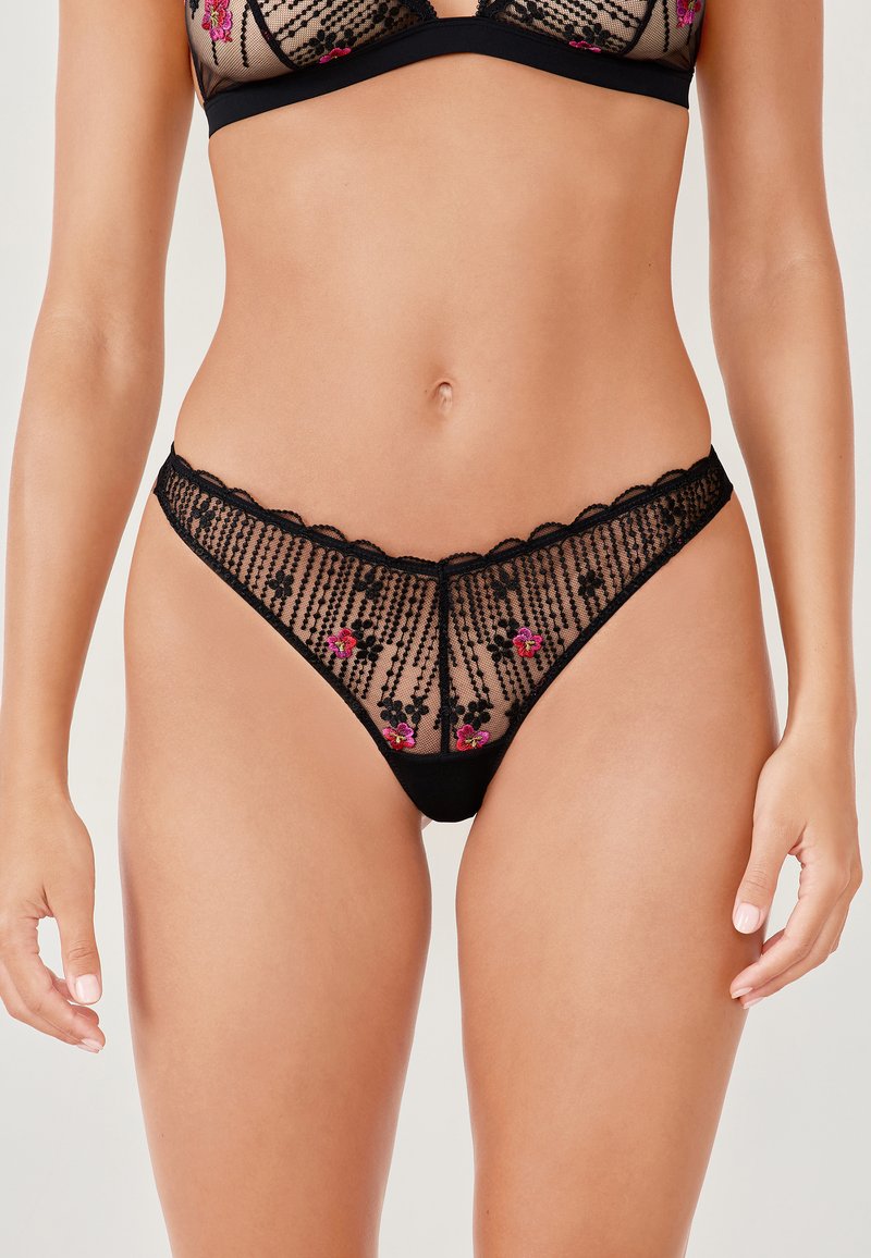 Black lace thong with floral embroidery in pink, featuring sheer mesh panels, a scalloped waistband, and vertical stripe detailing.