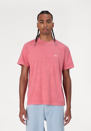 Tricou din bumbac roz, cu mâneci scurte și guler tip crew, având un mic logo alb "obey" pe partea stângă a pieptului.