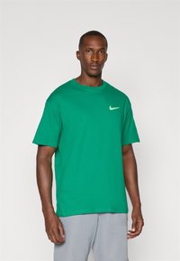 Green cotton T-shirt with short sleeves, round neckline, and a small white Nike logo on the upper left side. Smooth texture, casual fit.